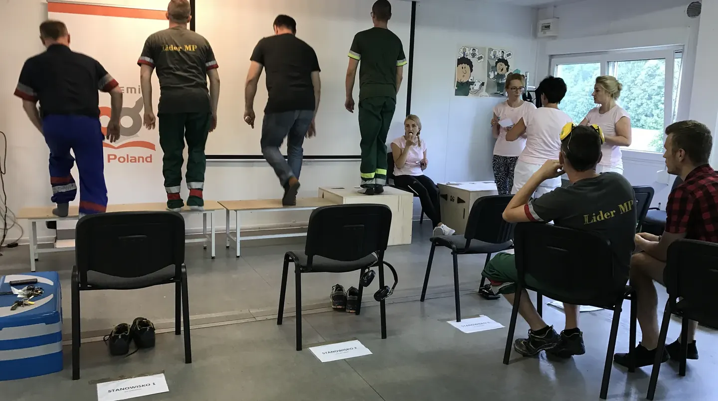 Pracownicy produkcji w odzieży roboczej podczas warsztatu ergonomii w zakładzie